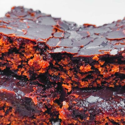3 slices of Gluten free Jam Cake stacked on top of each other, with a broken cacao topping that is dripping over the cake