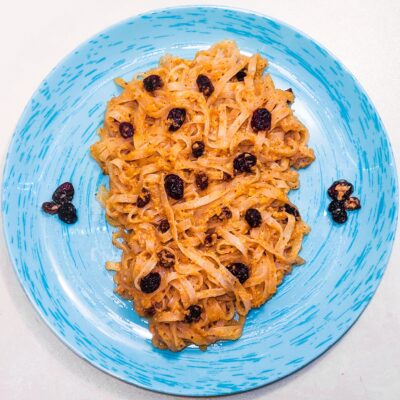 A top down view of some dessert noodles, served on a plate and topped with cranberries and dried fruits