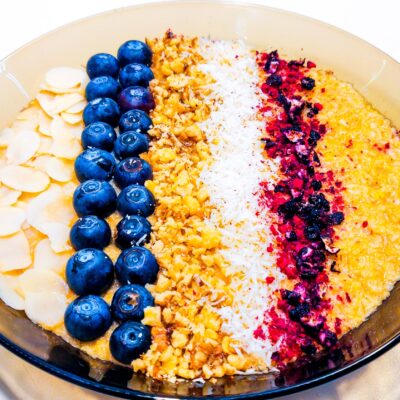 A front view of a plate containing a coconut porridge, topped with almond flakes, blueberries, ground walnuts, coconut flakes and dried fruits